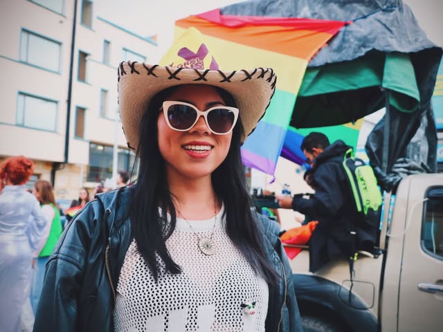 Le Viasus con sombrero y gafas, sonriendo en una celebración del orgullo